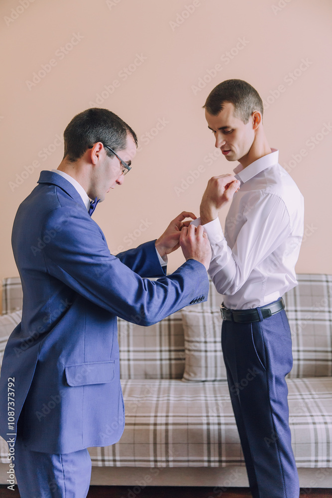 Two men are getting dressed up, one of them is wearing a blue suit and the other is wearing a white shirt Two men are getting dressed up, one of them is wearing a blue suit and the other is wearing a white shirt