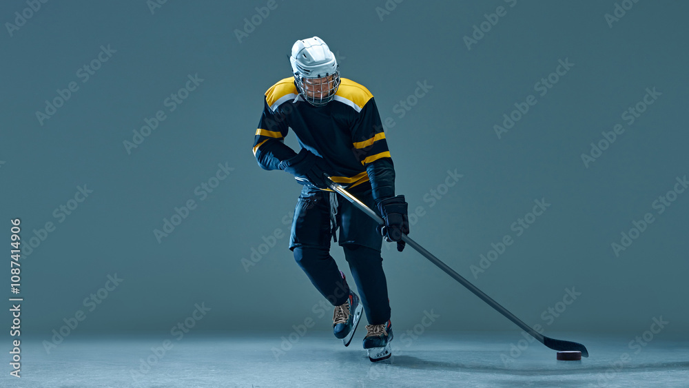 Obraz premium Man, ice hockey athlete in black and yellow uniform during powerful game on ice, captured in athletic stance against studio background. Concept of sport, game, tournament, action, competition