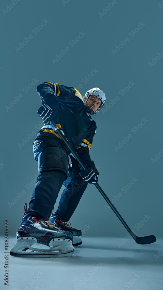 Fototapeta premium Vertical full-length image of concentrated man, hockey player in helmet and uniform, standing with stick, preparing for intensive game. Concept of sport, game, tournament, action, competition