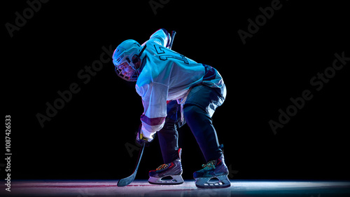 Photography Man, professional hockey player dressed in white, standing into powerful skating stance on ice against black studio background in neon light