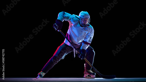Canvas Print Determined athlete, hockey player in white uniform in motion during game, controlling puck with stick against black studio background in neon light