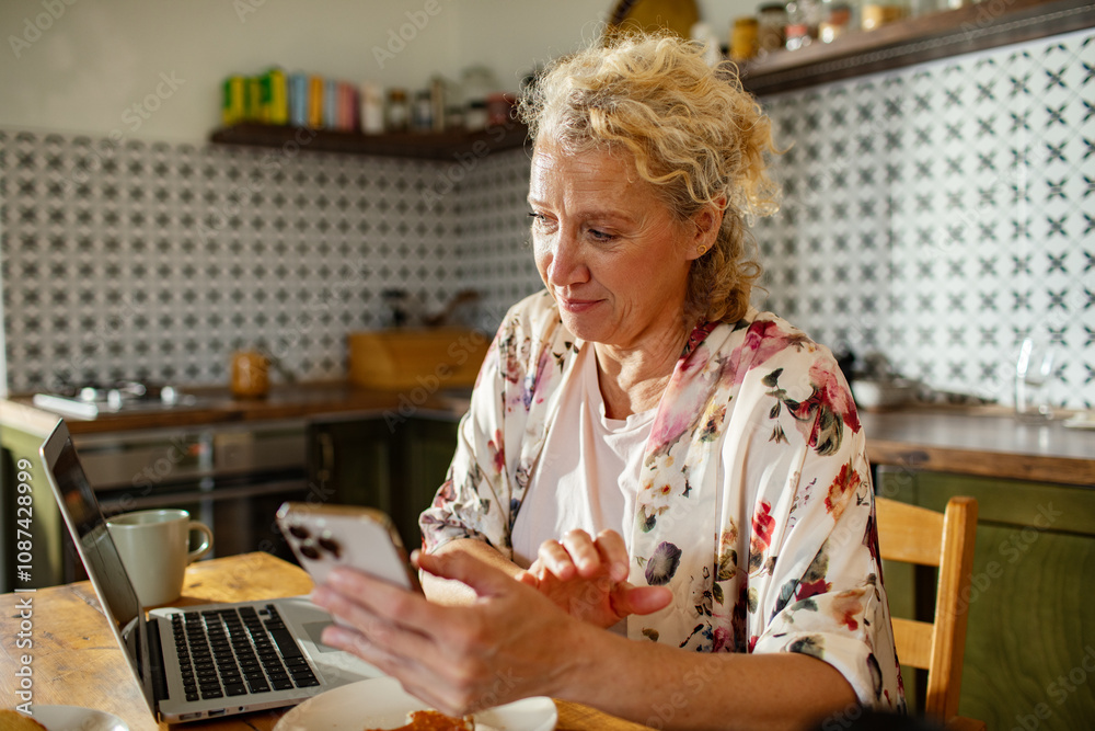 Middle aged woman using smartphone at kitchen desk at home Middle aged woman using smartphone at kitchen desk at home
