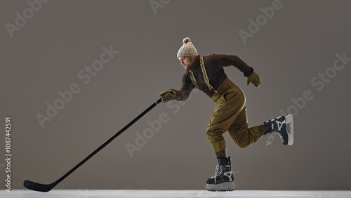 Photography Side view dynamic image of man in pant with suspenders, knitted hat and sweater, in motion with stick, playing hockey
