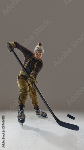 Photography Man wearing pants with suspenders, knitted warm sweater and hat, in motion with stick, hitting puck