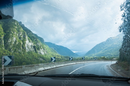 A wet road on a cloudy and rainy day seen from inside a vehicle. There is a sharp curve well signposted. Concept of driving, transportation and caution on the road