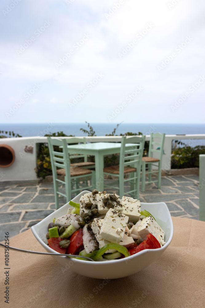 Delicious farmers salad called Horiatiki and a table in front of the blue Aegean sea during summer time as greek food concept.