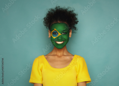 Portrait of a woman with the flag of Brazil painted on her face. Football or soccer team fan, sport event, faceart and patriotism concept. Studio shot at blue background, copy space photo