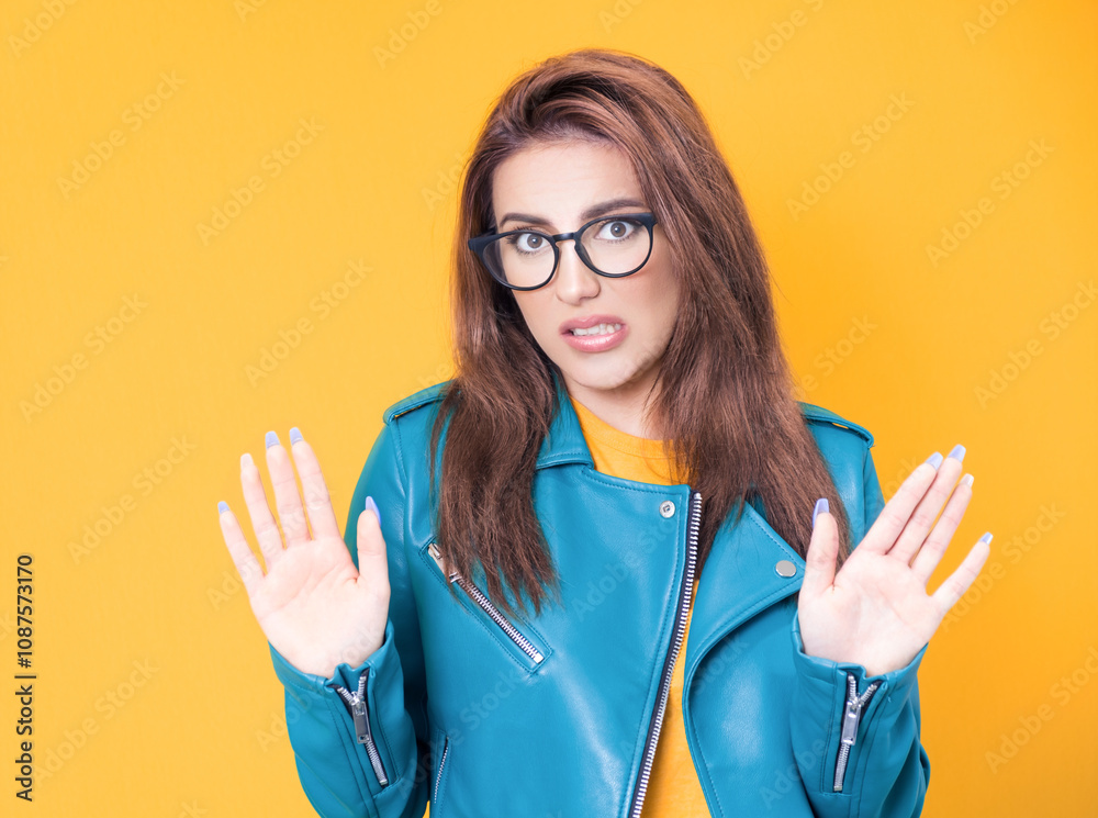 Young woman gesturing stop sign with palm of hand, refuses or reject something, wearing blue leather jacket, isolated on yellow background Young woman gesturing stop sign with palm of hand, refuses or reject something, wearing blue leather jacket, isolated on yellow background