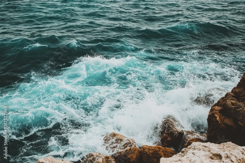 Waves crashing against rocky shore, creating foam and splashes in a serene ocean setting.