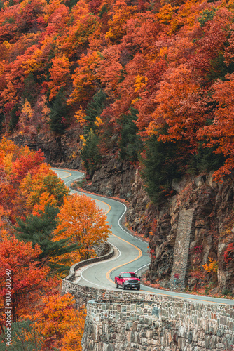 Bild auf Leinwand A red truck truck driving through windy roads in upstate New York during the fall foliage with trees bursting with color