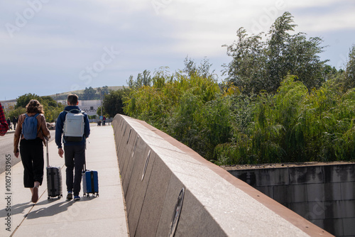 travelers crossing a bridge with their wheeled suitcases