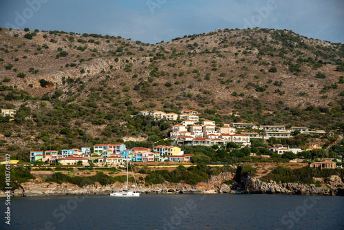 Colorful resort nestled on the coast of a greek island with sailboat moored offshore photo