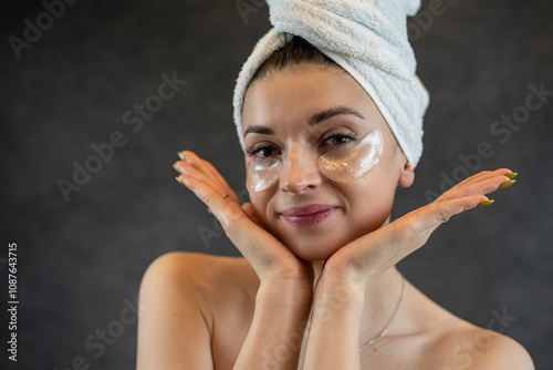 Cheerful woman in white towel applied collagen patch for smoothing skin under eye isolated on black photo