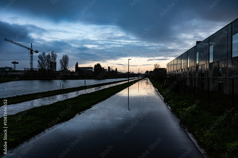 Obraz premium Colorful sunset and rain reflections at the industrial banks of the canal in Ruisbroek, Sint Pieters Leeuw, Belgium
