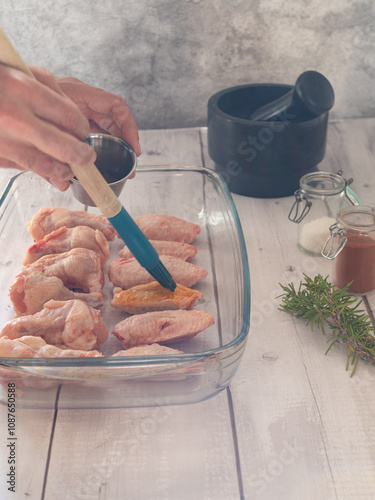 cook preparing chicken wings with barbecue sauce. white wooden table and cooking utensils.