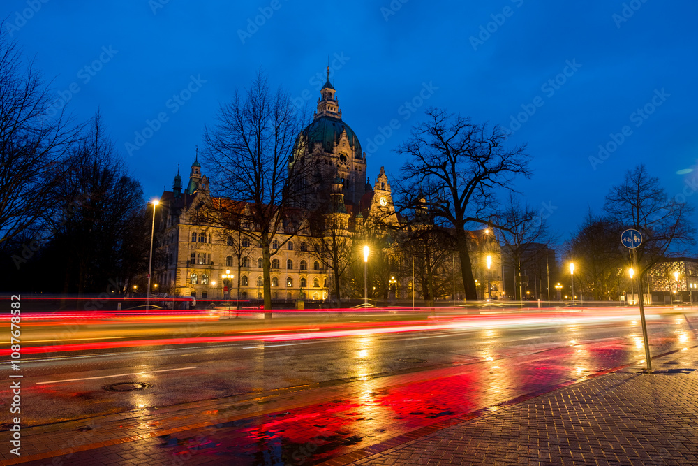 Obraz premium Hanover, Germany. The New Town Hall in Hanover, Germany at sunrise. Time-lapse of the road and illuminated landmark with cloudy sky in the morning