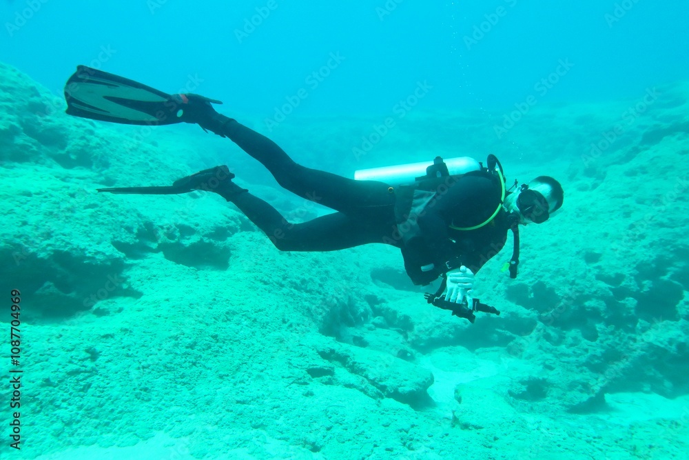 Scuba diver underwater, looking into the camera. Deeper rocky seascape, clear sea and swimming underwater explorer. Travel picture, adventure scuba trip. Seabed exploration, diver in the ocean. Scuba diver underwater, looking into the camera. Deeper rocky seascape, clear sea and swimming underwater explorer. Travel picture, adventure scuba trip. Seabed exploration, diver in the ocean.