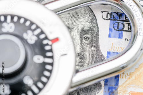 Financial or cyber security, fraud prevention, safeguarding assets and secure transactions : A combination of a US 100 dollar bill featuring Benjamin Franklin partially obscured by a combination lock.