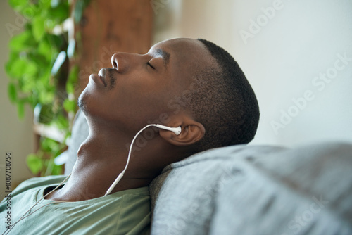 Young African man listening to music on earphones on his sofa photo