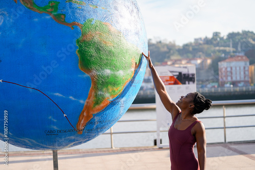 Young black woman touching giant earth globe promoting environmental awareness photo