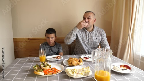 Father and son are sitting at the table, eating food and drinking drinks.