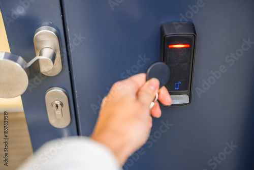 Close up view of person using a electric lock key fob to access a building via a reader of entry system mounted on a house wall