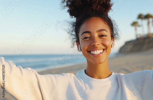A joyful young woman enjoys music at the beach under a bright blue sky in the...