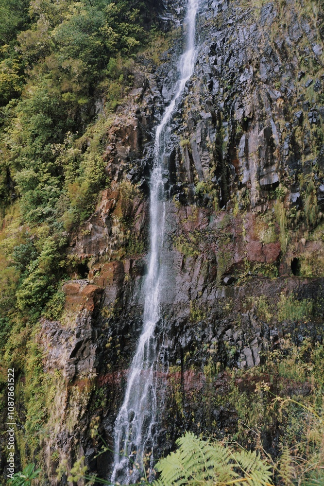 Obraz premium Majestic Waterfall Cascading Down Rocky Cliff Surrounded by Greenery