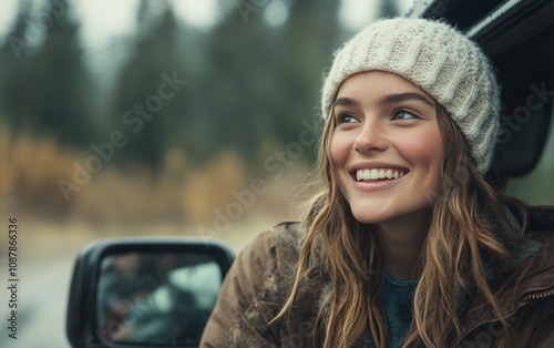Young woman smiles happily while leaning out of a car in a forest during autumn