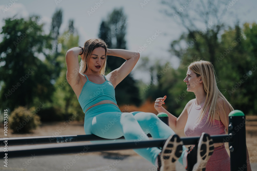 Two friends exercising together in a park, performing sit-ups using exercise equipment. They enjoy the sunny weather while focusing on fitness and motivation in an outdoor setting. Two friends exercising together in a park, performing sit-ups using exercise equipment. They enjoy the sunny weather while focusing on fitness and motivation in an outdoor setting.