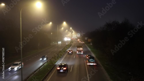 A foggy evening on a busy highway illuminated by streetlights. Cars with bright headlights and taillights are moving swiftly in both directions, creating a serene yet dynamic urban scene. photo