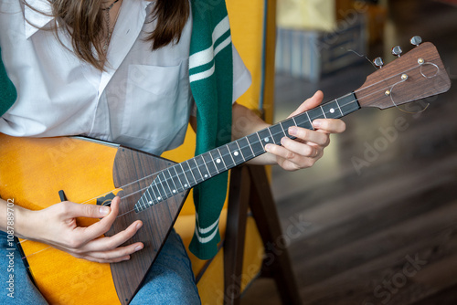 Fotografie Young woman playing on Russian balalaika at home, closeup view on hands and strings
