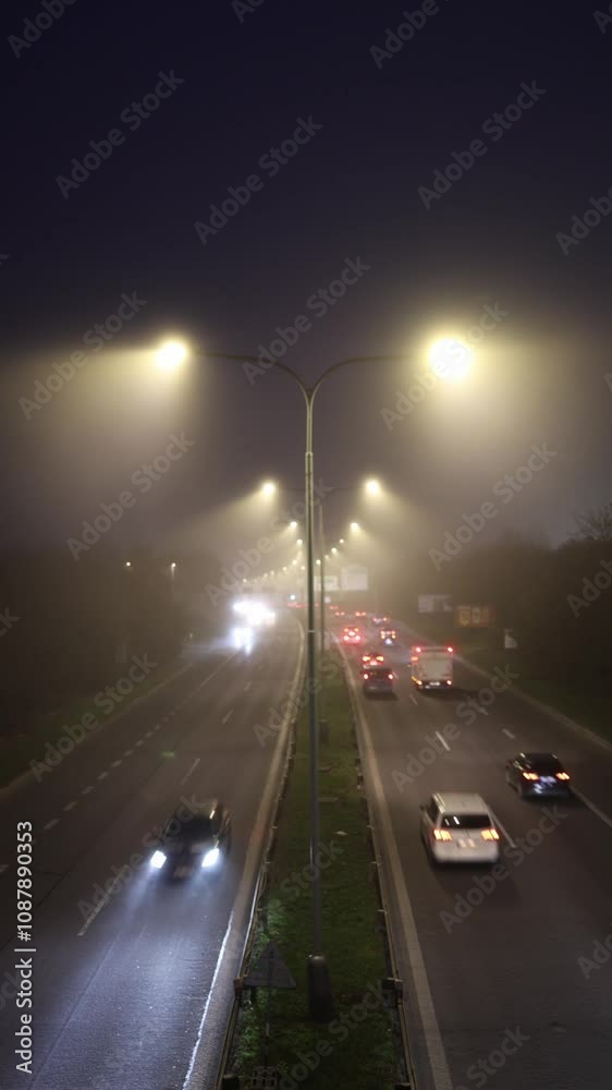 People are driving home from work, creating heavy traffic on a foggy highway illuminated by glowing streetlights, capturing the bustling rhythm of urban life