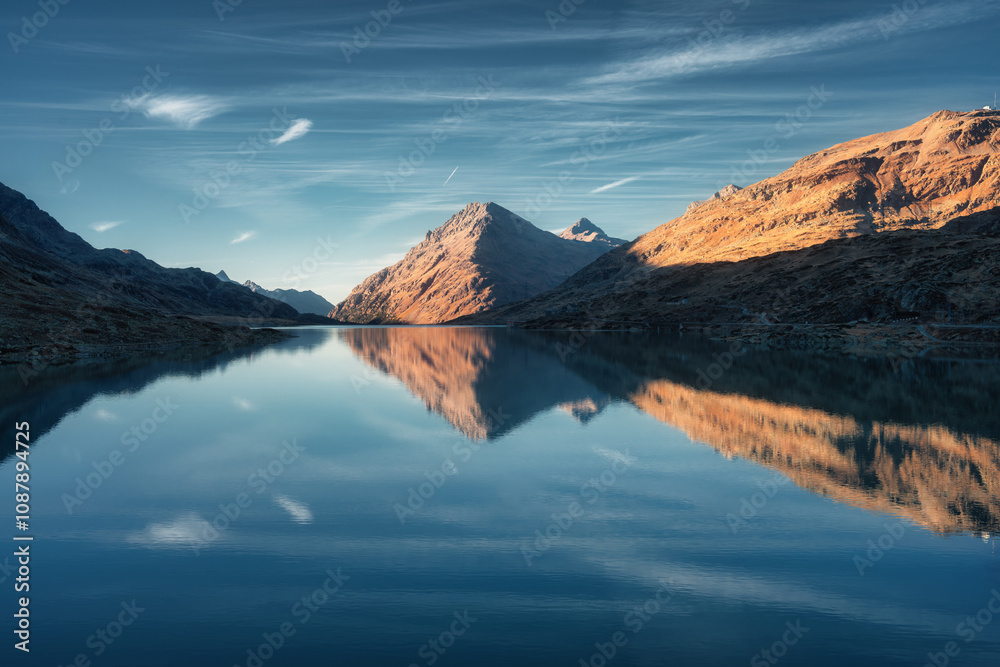 Obraz premium Sunset casts a serene glow on mountain peaks mirrored in a tranquil alpine lake in autumn. Lake Bianco, Switzerland in fall. Landscape with mountains, reflection in water, blue sky. Picturesque scene