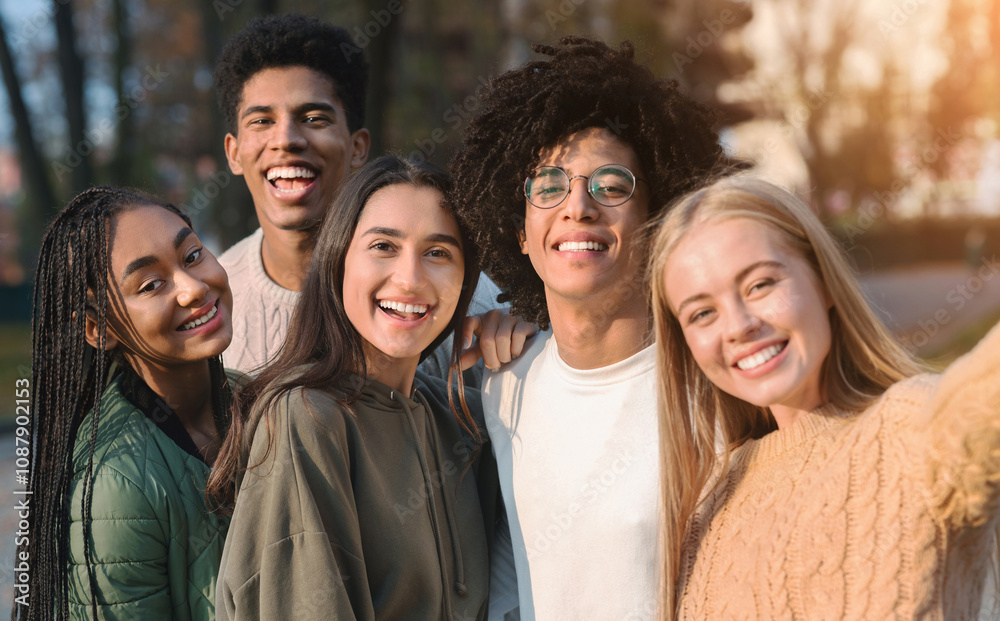 Positive international teen friends taking selfie while walking in autumn park Positive international teen friends taking selfie while walking in autumn park