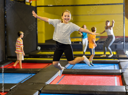 Expressive carefree tween girl having fun during free-jumping session in indoor trampoline arena..