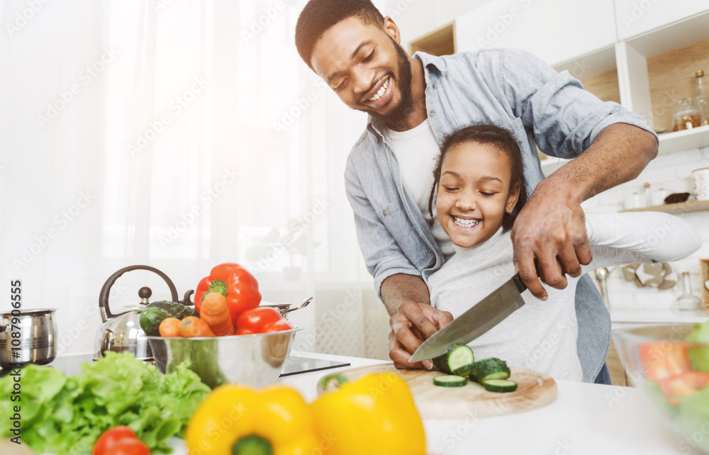 Afro man teaching his little daughter to cut vegetables, cooking salad. Family cooking school concept, copy space Afro man teaching his little daughter to cut vegetables, cooking salad. Family cooking school concept, copy space