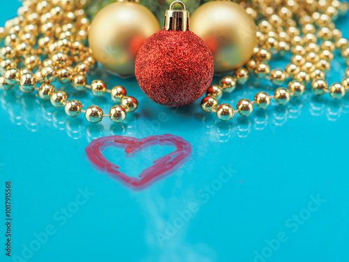 Red heart painted on blue glass surface, red and gold decoration balls and golden beads garland and small green tree in the background. Celebrating New Year and Christmas concept. photo