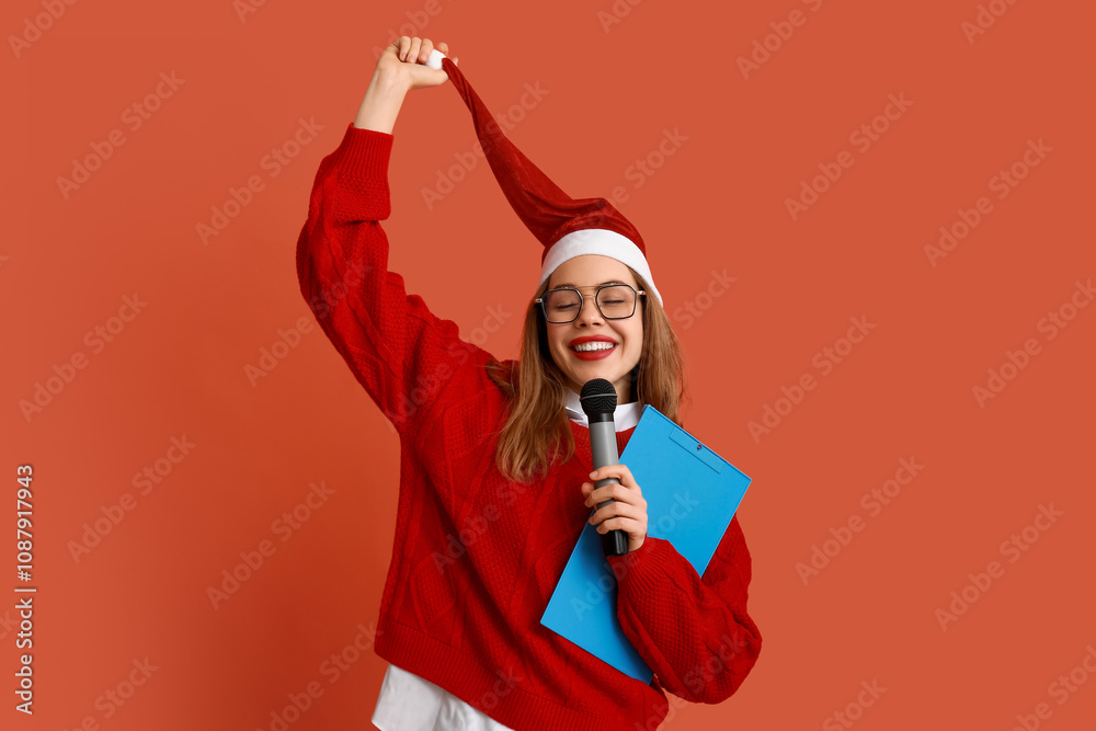 Young female journalist in Santa hat on red background Young female journalist in Santa hat on red background