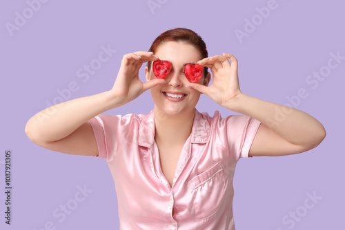 Beautiful young woman covering eyes with heart-shaped soap bars on lilac background