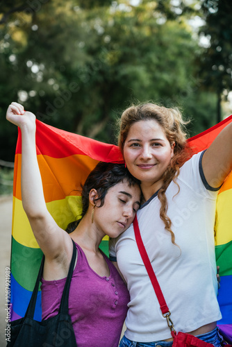 Two young women embracing while holding lgbt flag