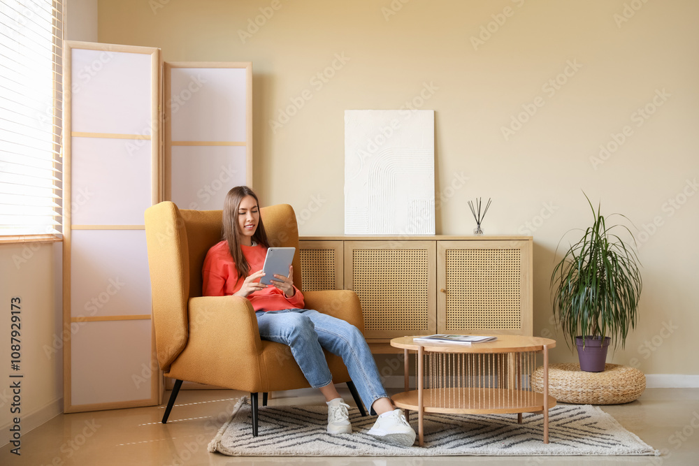 Young woman using tablet computer while sitting in armchair in room Young woman using tablet computer while sitting in armchair in room