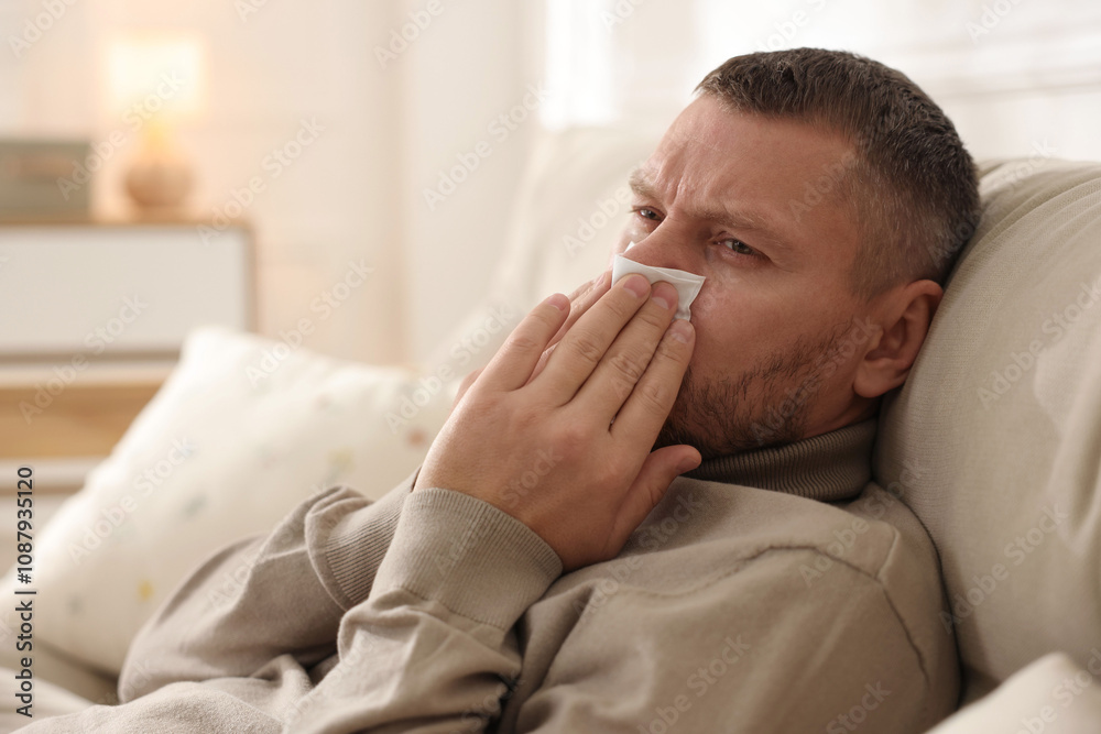 Man with tissue blowing runny nose at home. Space for text Man with tissue blowing runny nose at home. Space for text