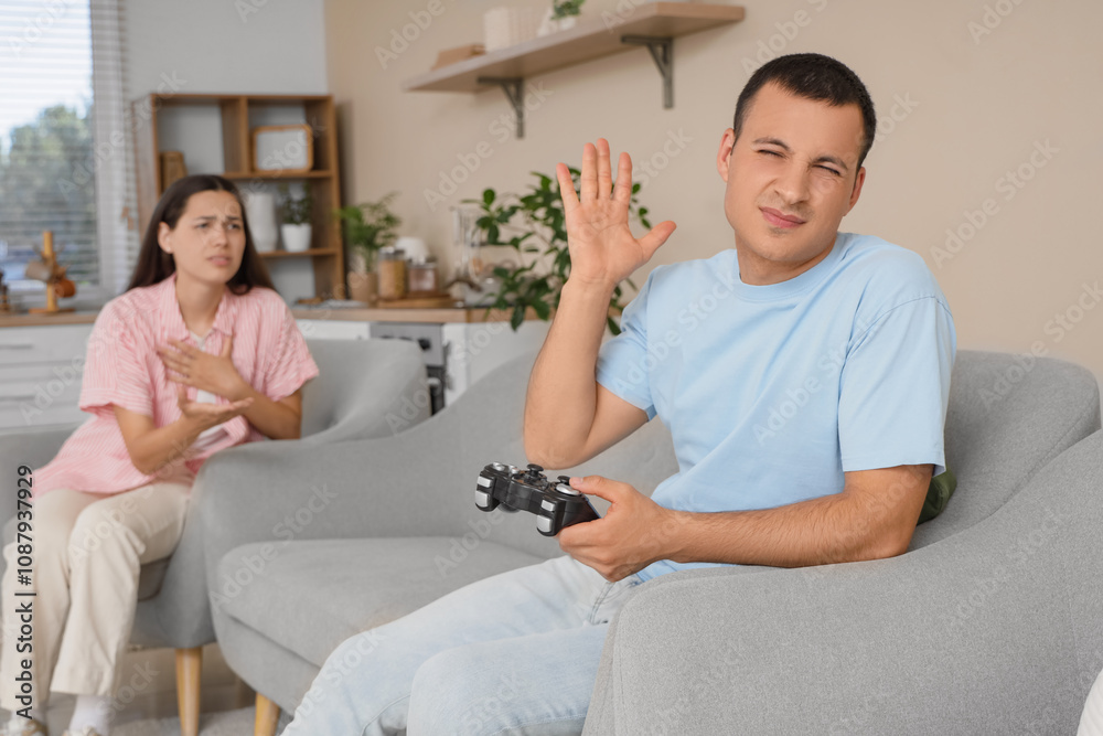 Young man playing video game and his quarreling wife at home Young man playing video game and his quarreling wife at home