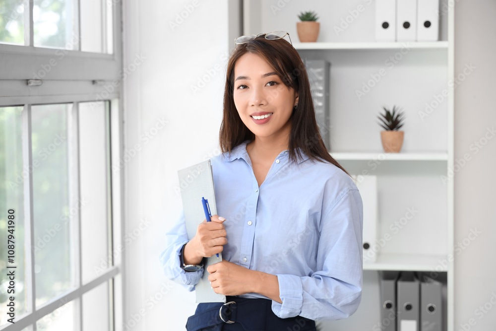 Asian businesswoman with clipboard near window in office Asian businesswoman with clipboard near window in office