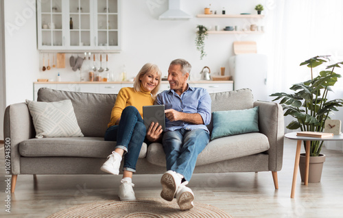 Cheerful Mature Spouses Using Digital Tablet Browsing Internet Or Watching Movie Together Sitting On Couch At Home. Senior People And Gadgets, Retirement Lifestyle Concept