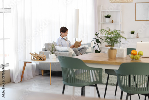 Young woman reading book on sofa in dining room