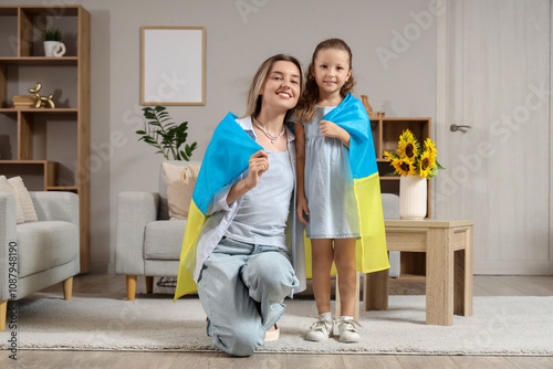 Cute little girl and her mother with Ukrainian flag at home photo