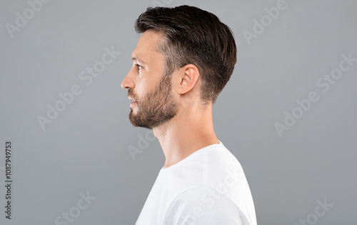 Obraz na płótnie Profile portrait of middle-aged bearded man in white t-shirt over grey studio background, copy space
