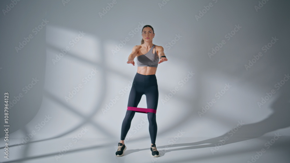 Motivated lady making squats at empty room. Woman using fitness band training Motivated lady making squats at empty room. Woman using fitness band training